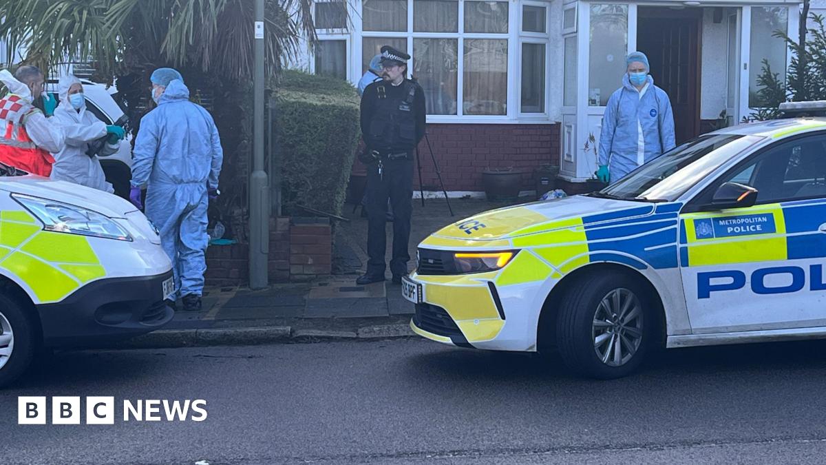 A semi-detached house with police cars parked outside. Three people in fill forensic suits are in view.
