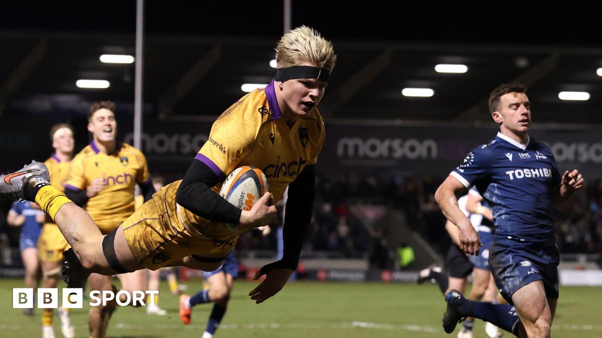 Henry Pollock, wearing a black headband, leaps in the air with the ball under his arm, to score Northampton's final try as Sale fly-half George Ford watches on