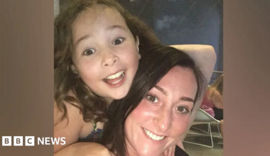 Milly Main smiling while looking at the camera. She has long brown hair. She is on the back of Kimberly Darroch, who has long black hair and is also smiling at the camera.