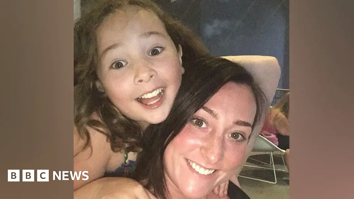 Milly Main smiling while looking at the camera. She has long brown hair. She is on the back of Kimberly Darroch, who has long black hair and is also smiling at the camera.