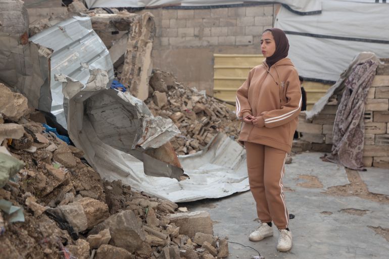 Batoul stands in front of the rubble of her destroyed home, where she was trapped for about an hour before being rescued when it was hit [Abdelhakim Abu Riash/ Al Jazeera]