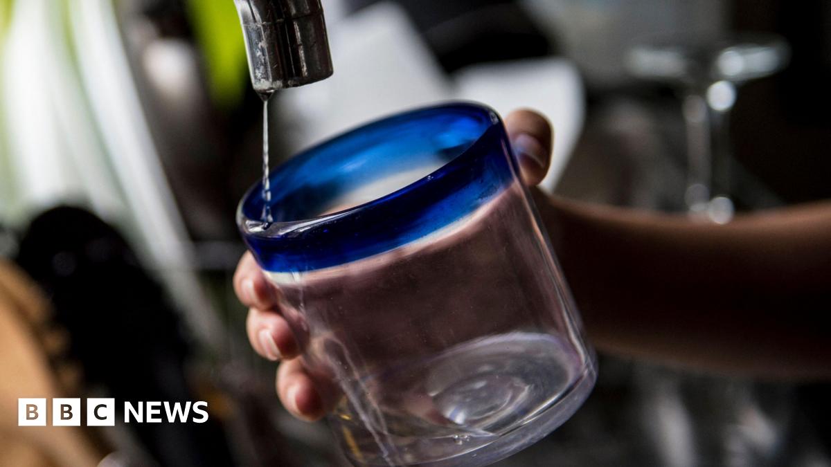 A hand holding a glass under a dripping tap