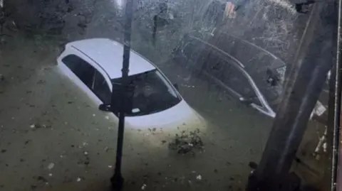 Supplied A white car is surrounded by water. The photo was taken at night from above. 