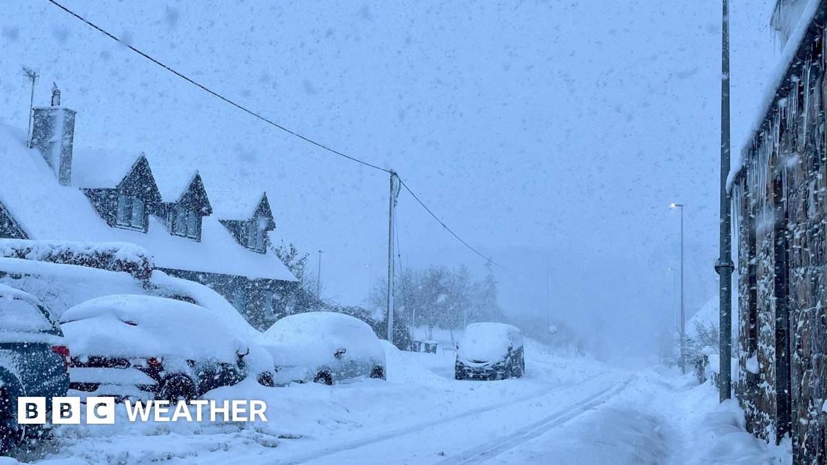 Street scene, with road, cars and houses covered in thick snow. Heavy snow is falling