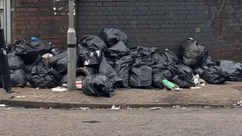 A large pile of black bin bags stacking up on a pavement 