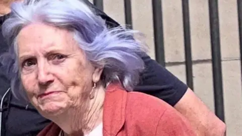 Alexander Lawrie woman with purple rinsed hair wearing a red top and pink T shirt pictured outside a court building
