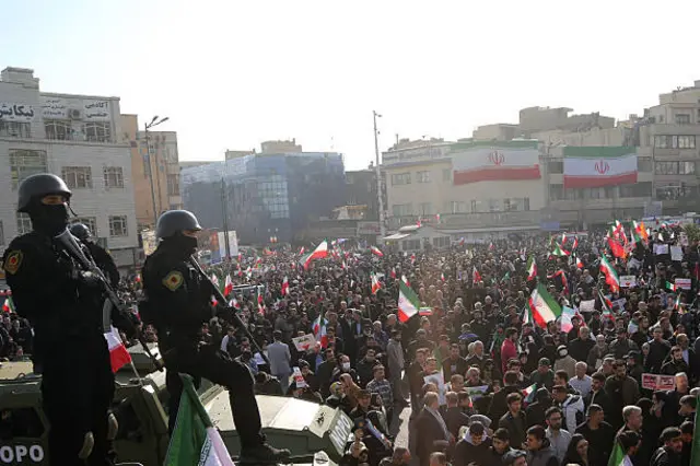 Security forces seen holding guns as people gather waving Iranian flags at a pro-government rally in Tehran