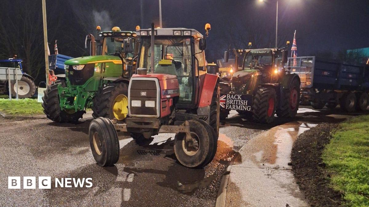 Multiple tractors are parked on a road, completely blocking access. One has a sign that says "Back British farming" on the front.