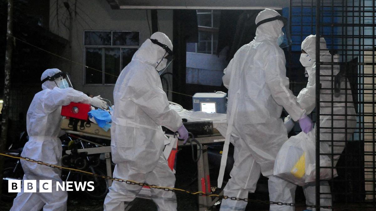 Four medical workers in white protective clothing move an unseen patient on a hospital trolley.