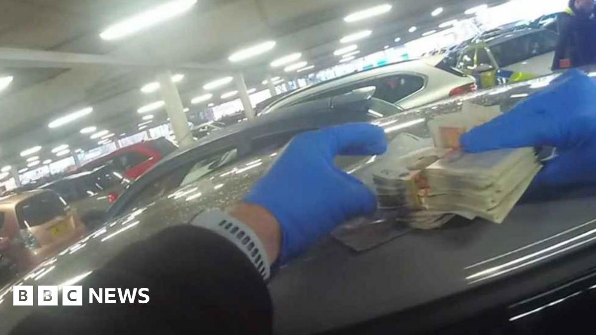 Police body cam footage showing a police officer wearing blue plastic gloves holding wads of cash
