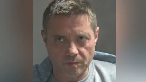Hertfordshire Police A custody photo of John Alford wearing a grey T-shirt or jumper.