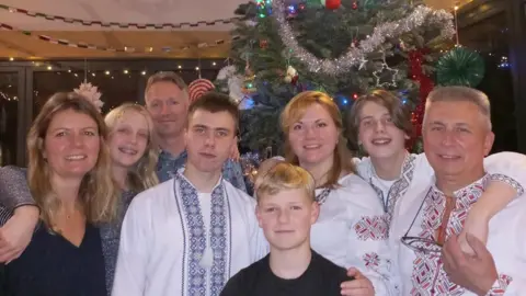 Steve Vinnicombe Two families, one wearing traditional Ukrainian clothes, are standing in front of a Christmas tree