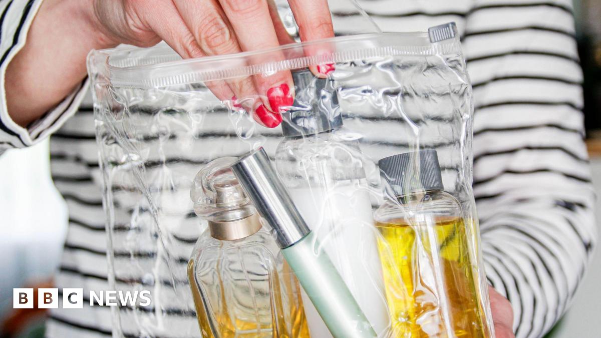 Woman's hand with red nail varnish places small bottles of toiletries in clear plastic bag