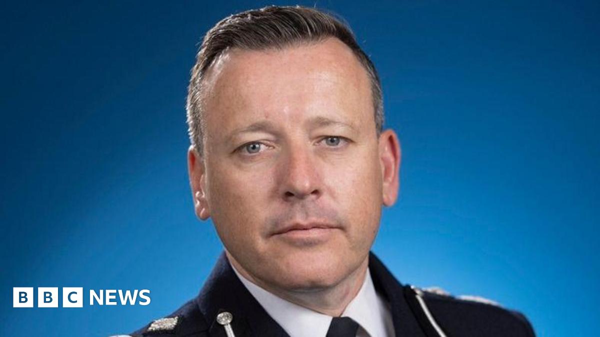 A close-up photo of the acting chief constable of West Midlands Police. He wears a black police uniform and stands in front of a blue background, looking into the camera.