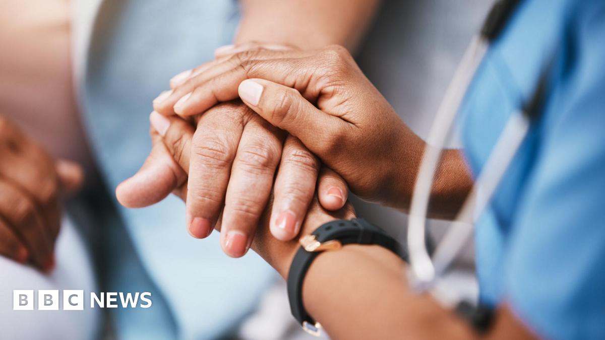 Millie Bobby Brown and David Harbour in character as Eleven and Jim Hopper. Eleven wears red shorts over grey leggings and a grey jumper. Jim Hopper wears a black leather jacket, a black beanie hat and dark trousers.They are speaking to director Frank Darabont on the set of Stranger Things. There is a vintage advertisement posted in the background with debrief on the ground.
