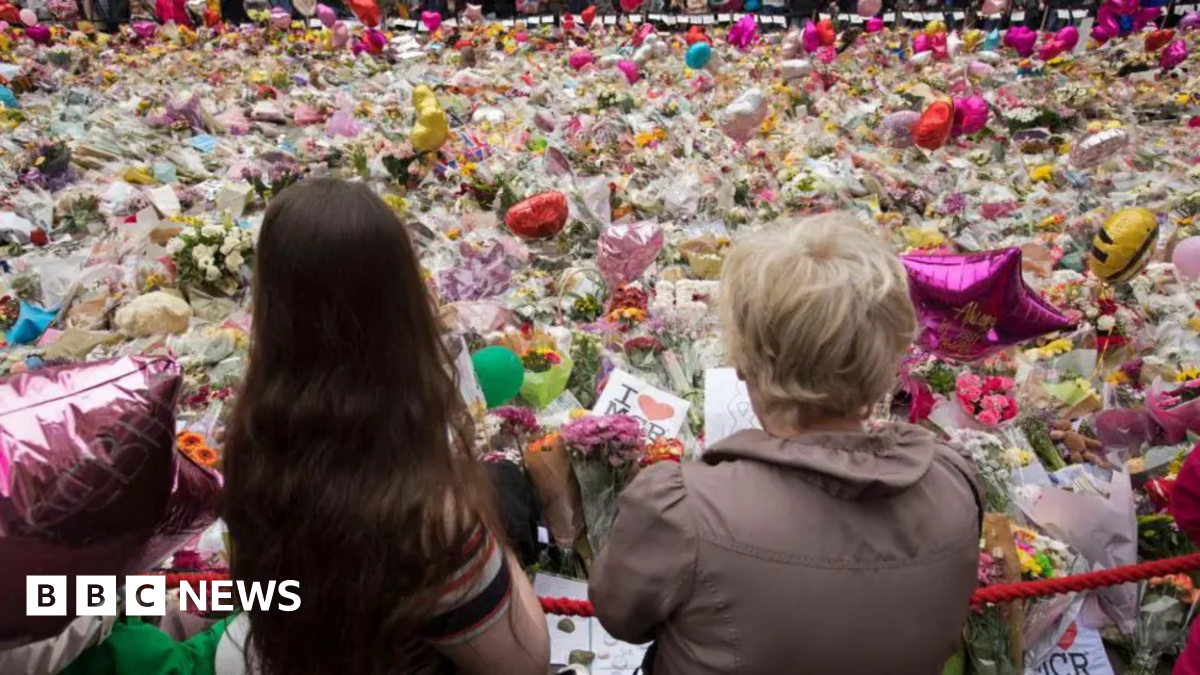 Two women stand in front of tributes to the victims of the Manchester Arena bombing in 2017
