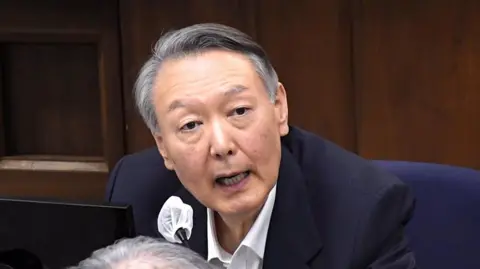 EPA/Shutterstock Yoon Suk Yeol with grey hair and a navy suit speaking into a microphone