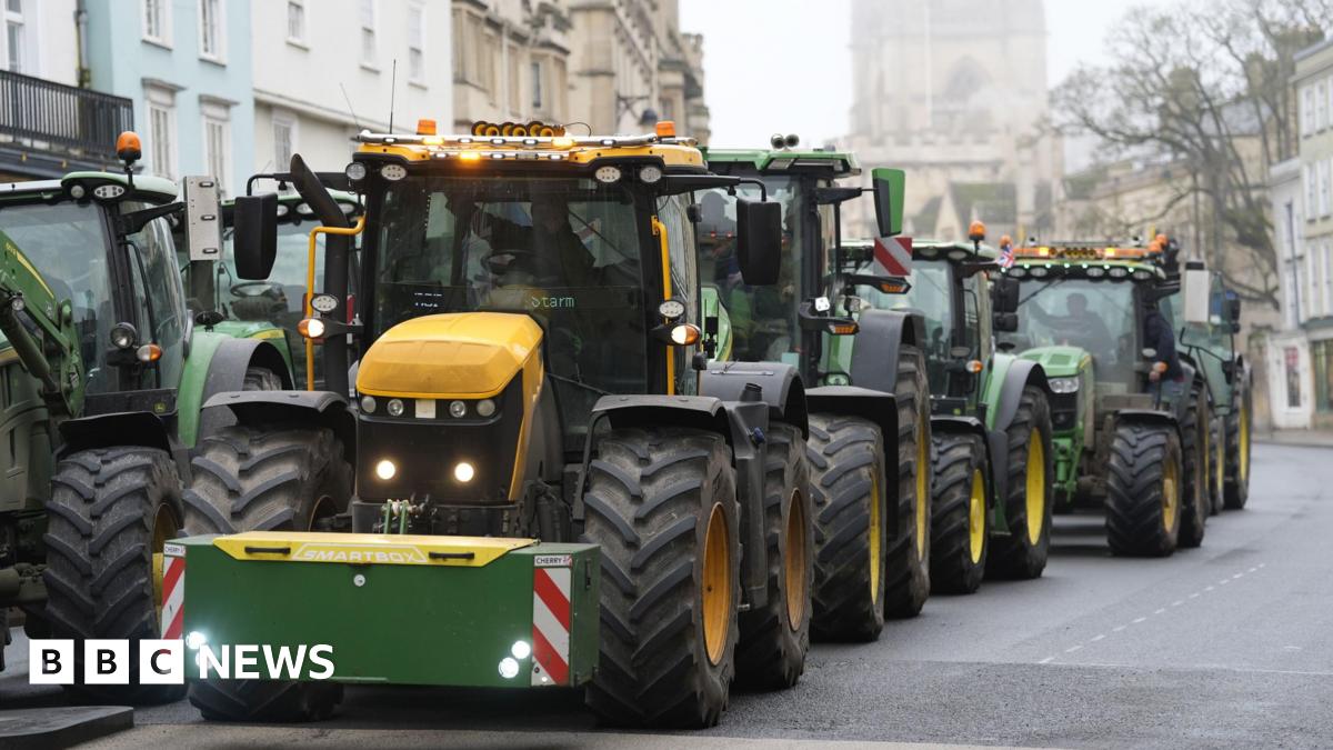 A queue of green and yellow tractors makes its way through an Oxford city centre road, with historic buildings in the background, under a misty sky
