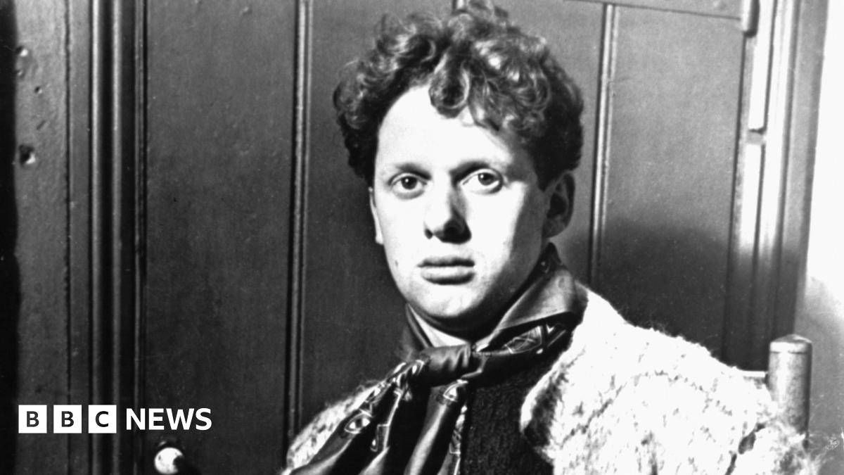 A black and white photo of a young Dylan Thomas, wearing a cravat and looking straight at the camera. He is sitting down and has short curly hair.
