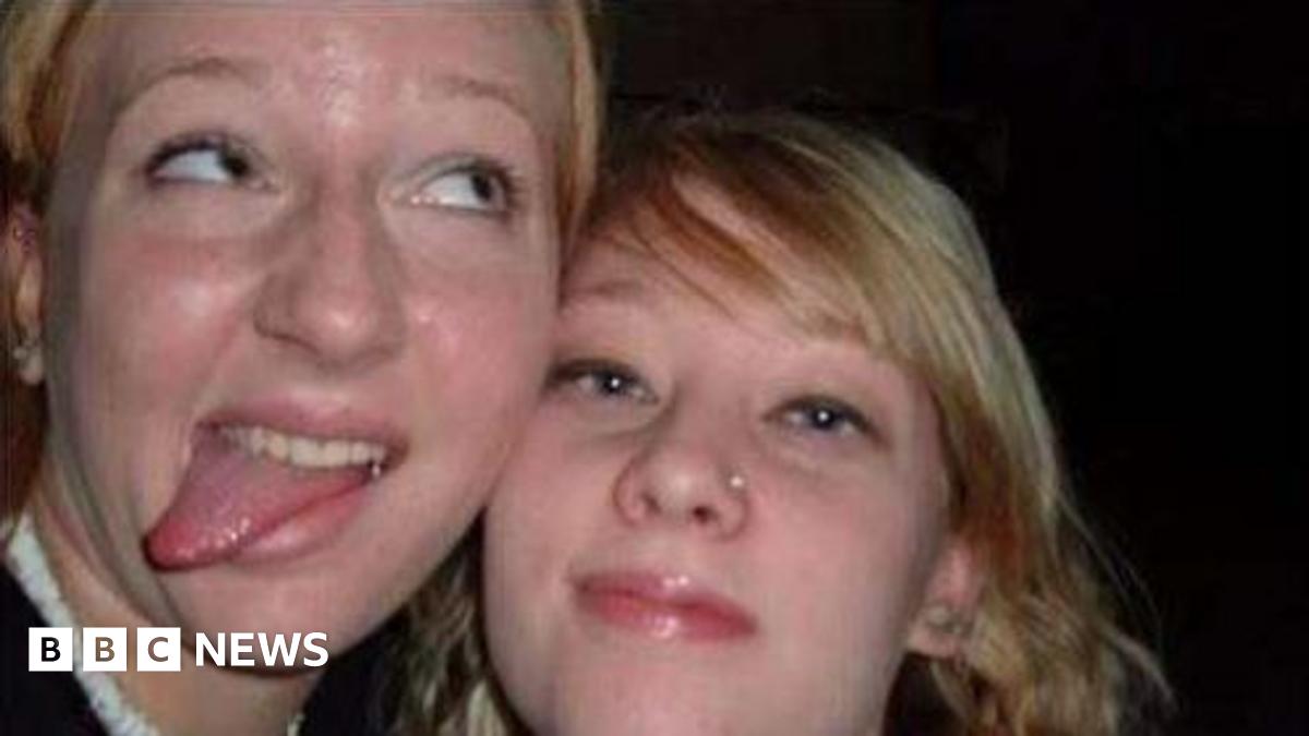 A close-up image of two young women looking into the camera. The woman on the left is looking off to the side and sticking her tongue out. The woman on the right is looking into the camera.