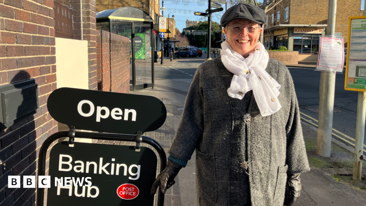 Woman with hat and scarf by a sign which says 'open' and 'banking hub'