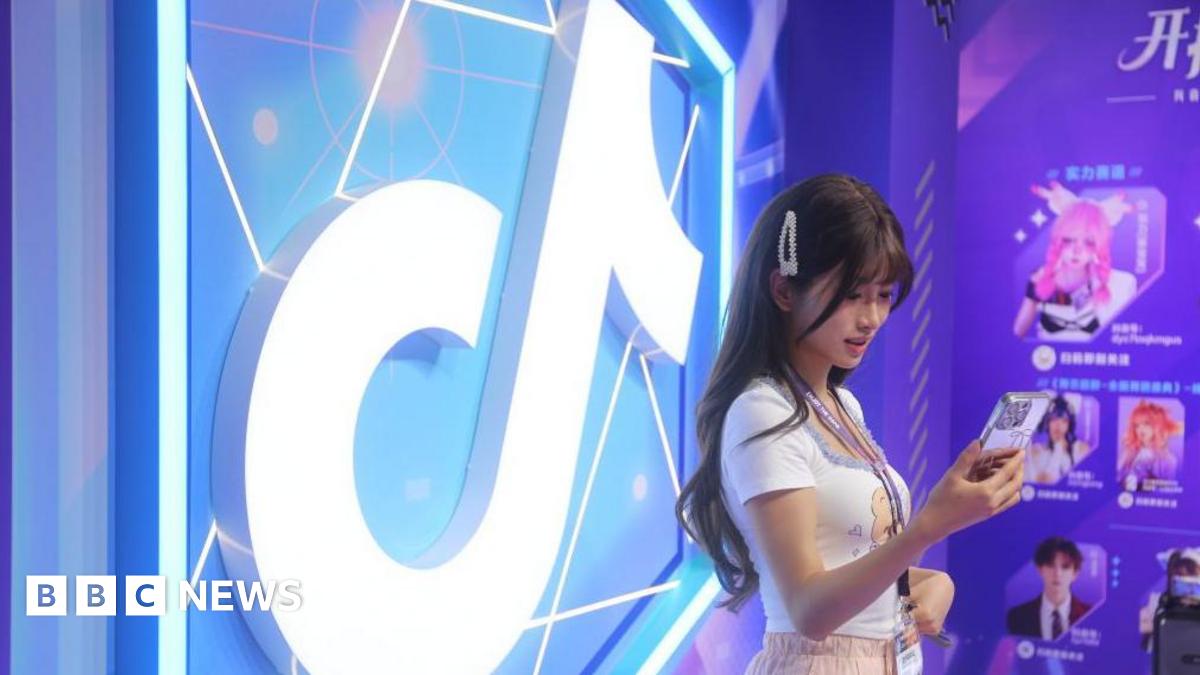 Woman standing in front of a brightly-lit and colourful TikTok logo while looking at her smartphone