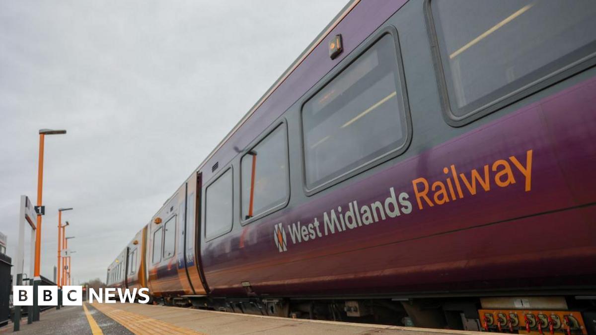 The side of train carriages pulled up on a platform. The words West Midlands Railway can be seen on one carriage