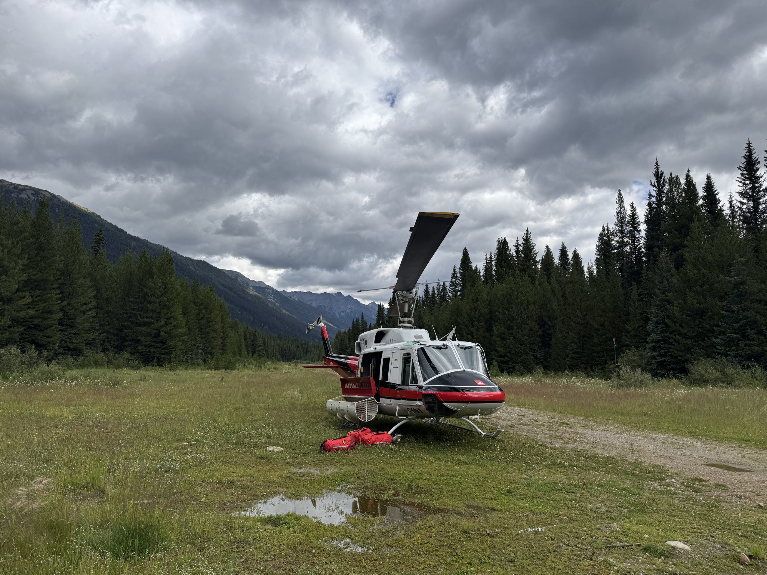 A helicopter sits on a grassy field in a mountainous area.