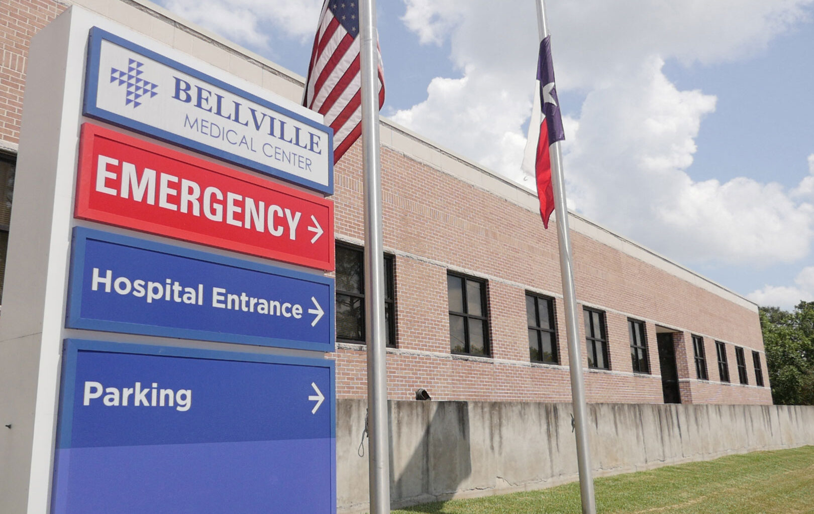 A photo of an emergency room sign for Bellville Medical Center. The American flag and the Texas flag are seen on poles next to it.