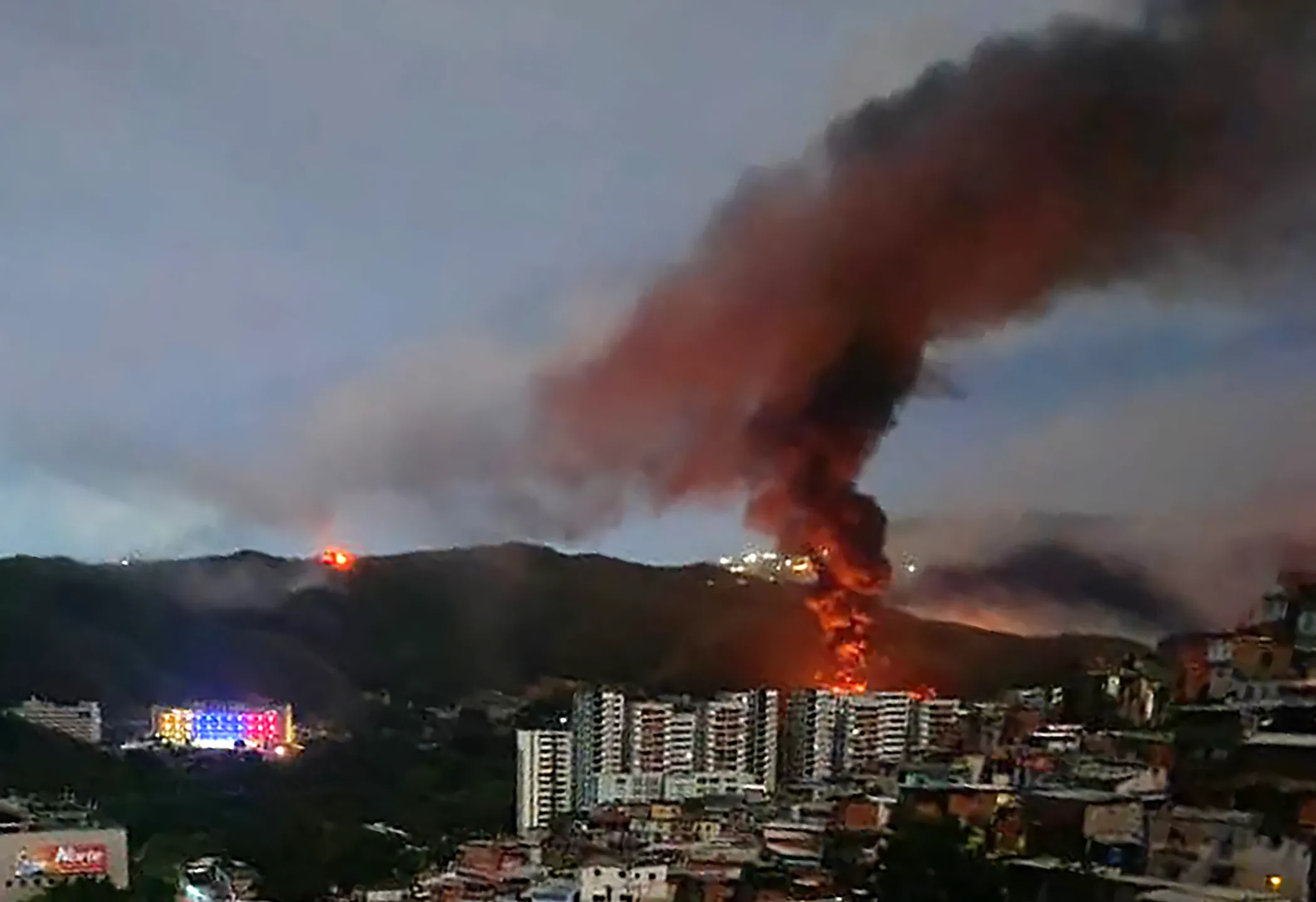 TOPSHOT - Fire at Fuerte Tiuna, Venezuela's largest military complex, is seen from a distance after a series of explosions in Caracas on January 3, 2026. The United States military was behind a series of strikes against the Venezuelan capital Caracas on Saturday, US media reported. The White House and Pentagon have not commented on the explosions and reports of aircraft over the city. US media outlets CBS News and Fox News reported unnamed Trump administration officials confirming that US forces were involved. (Photo by AFP via Getty Images)
