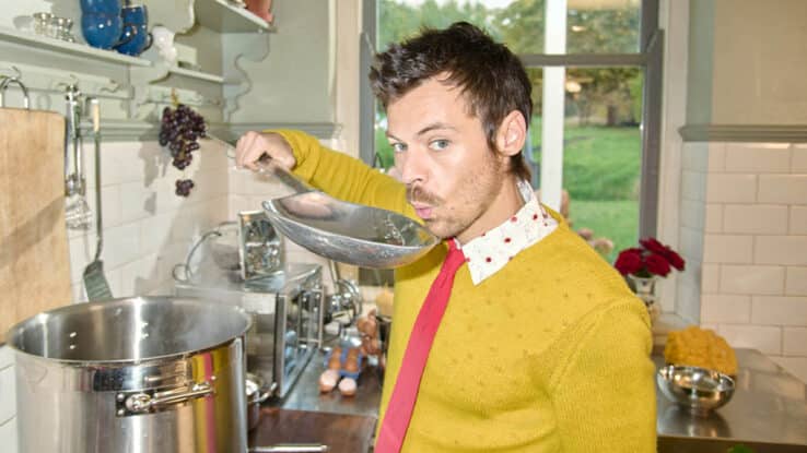 Harry Styles, blowing on a giant spoon to cool the contents, as he stands over a cooking stove