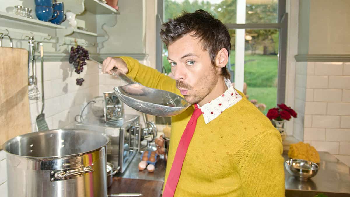 Harry Styles, blowing on a giant spoon to cool the contents, as he stands over a cooking stove