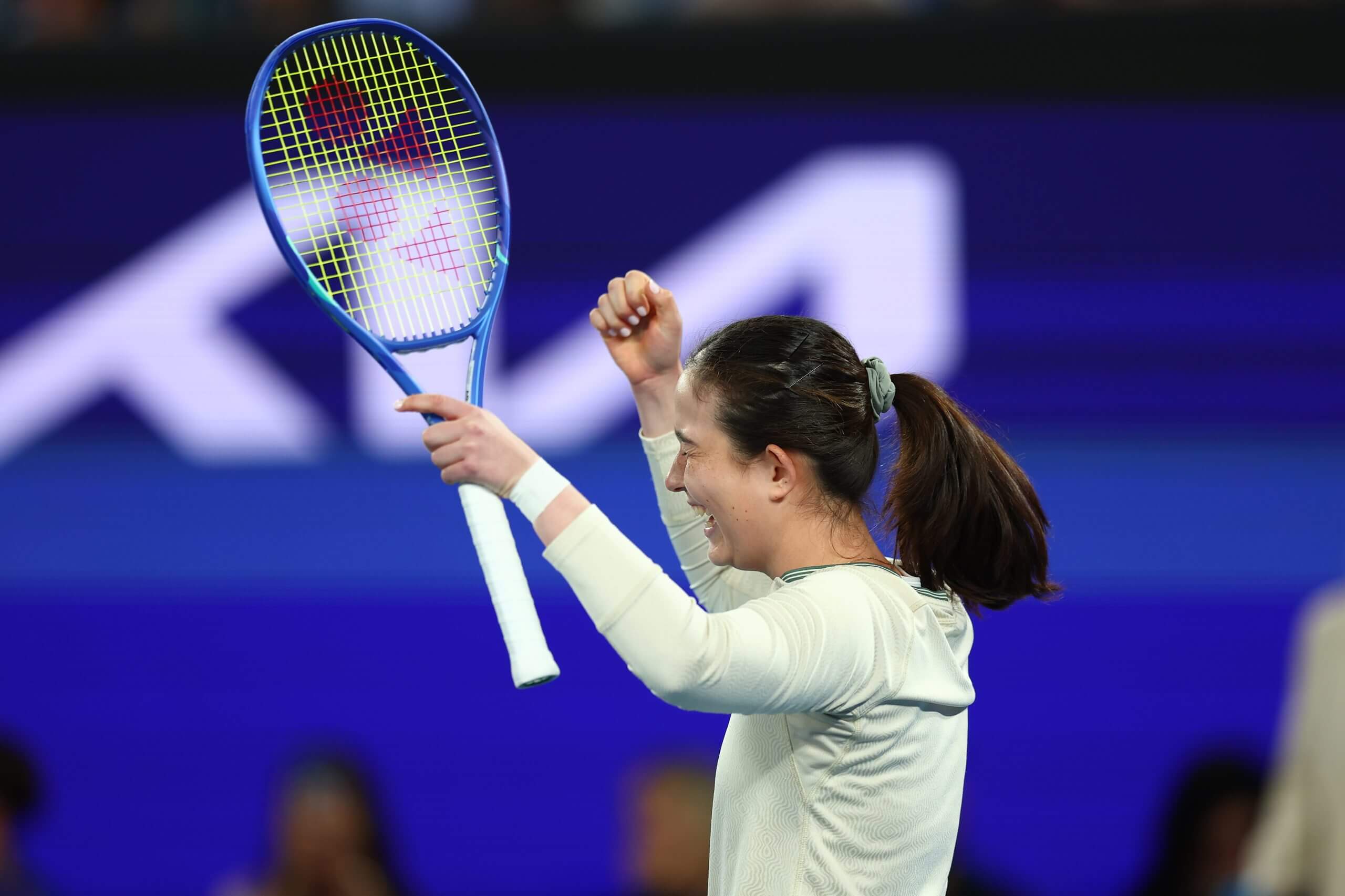 Joanna Garland raises her tennis racket and her right hand in celebration.