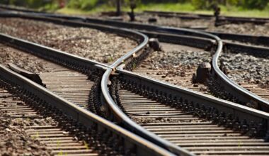 Close-up of railway tracks splitting into multiple directions on a gravel bed, showing a railway switch mechanism under bright daylight.