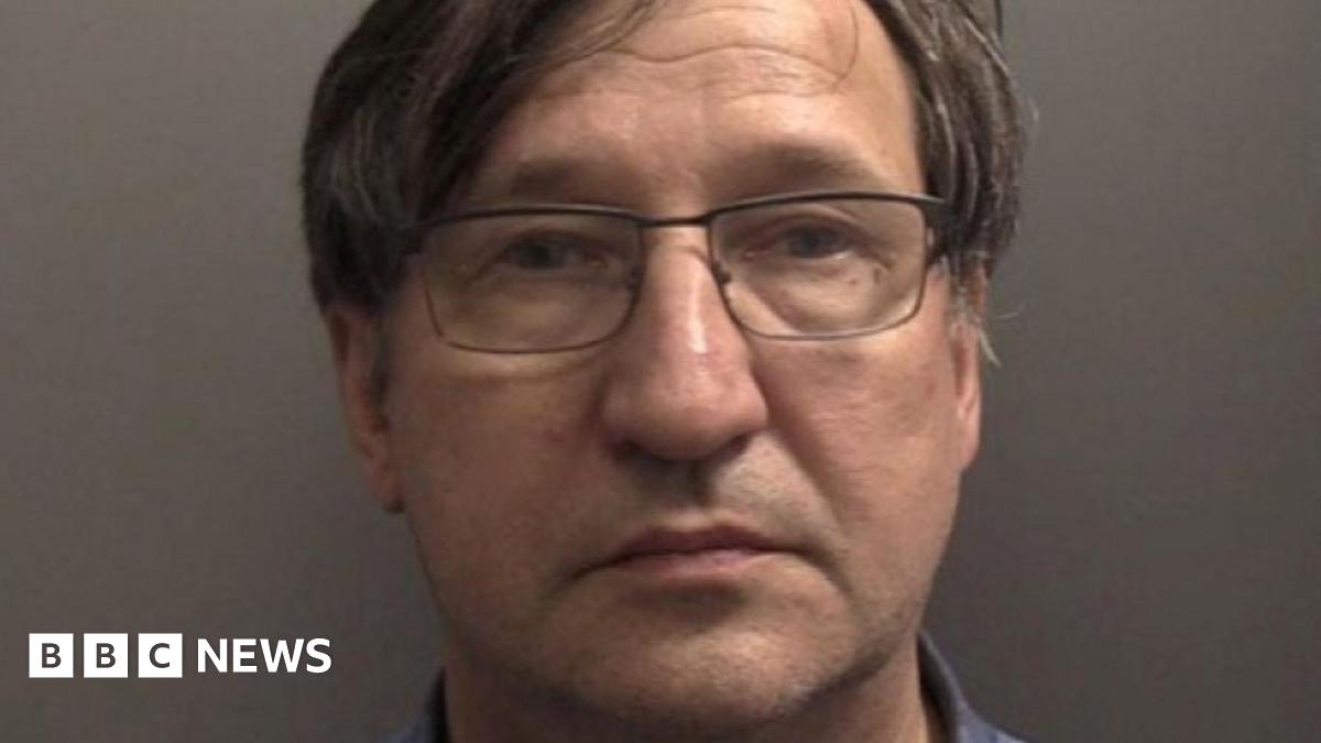Police custody picture of Vladimir Motin. He has short dark hair with a parting and is wearing glasses. He is staring into the camera against a grey wall.