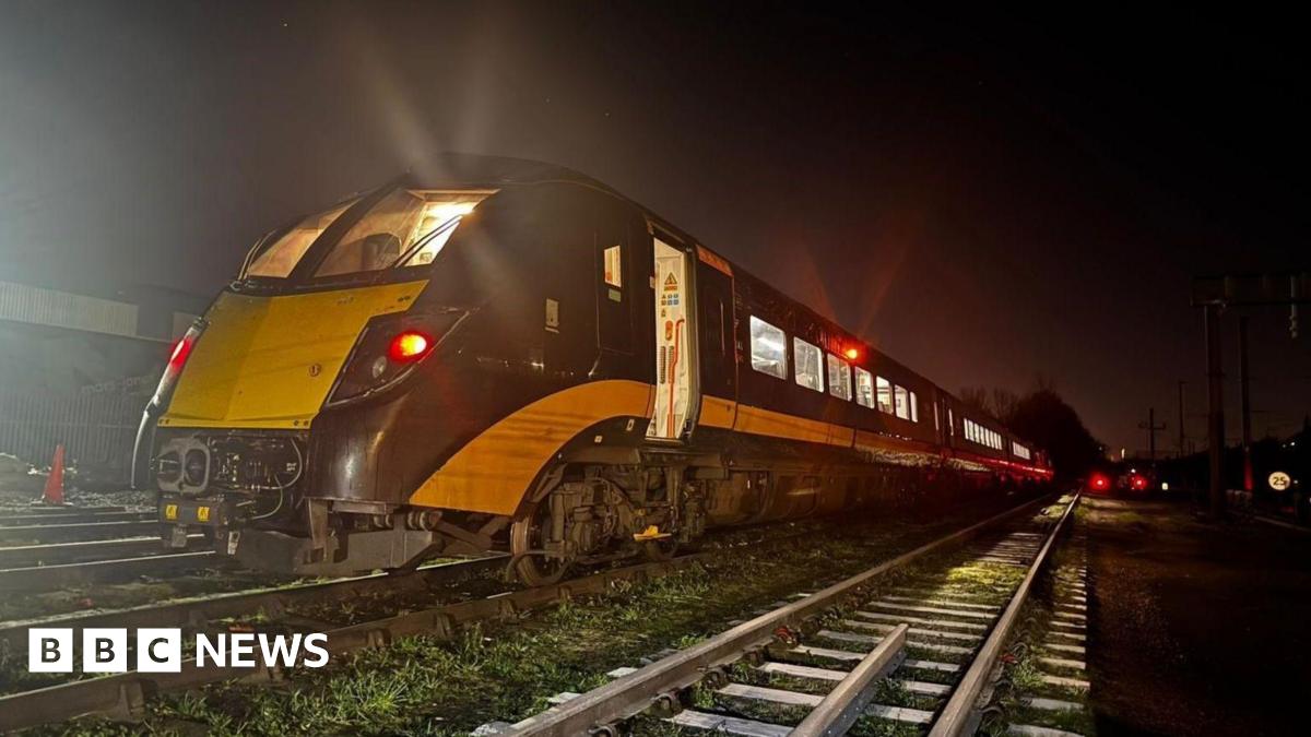 A train is on a railway in the dark. It is black and yellow and has its lights on. There is another track on the right of the image.