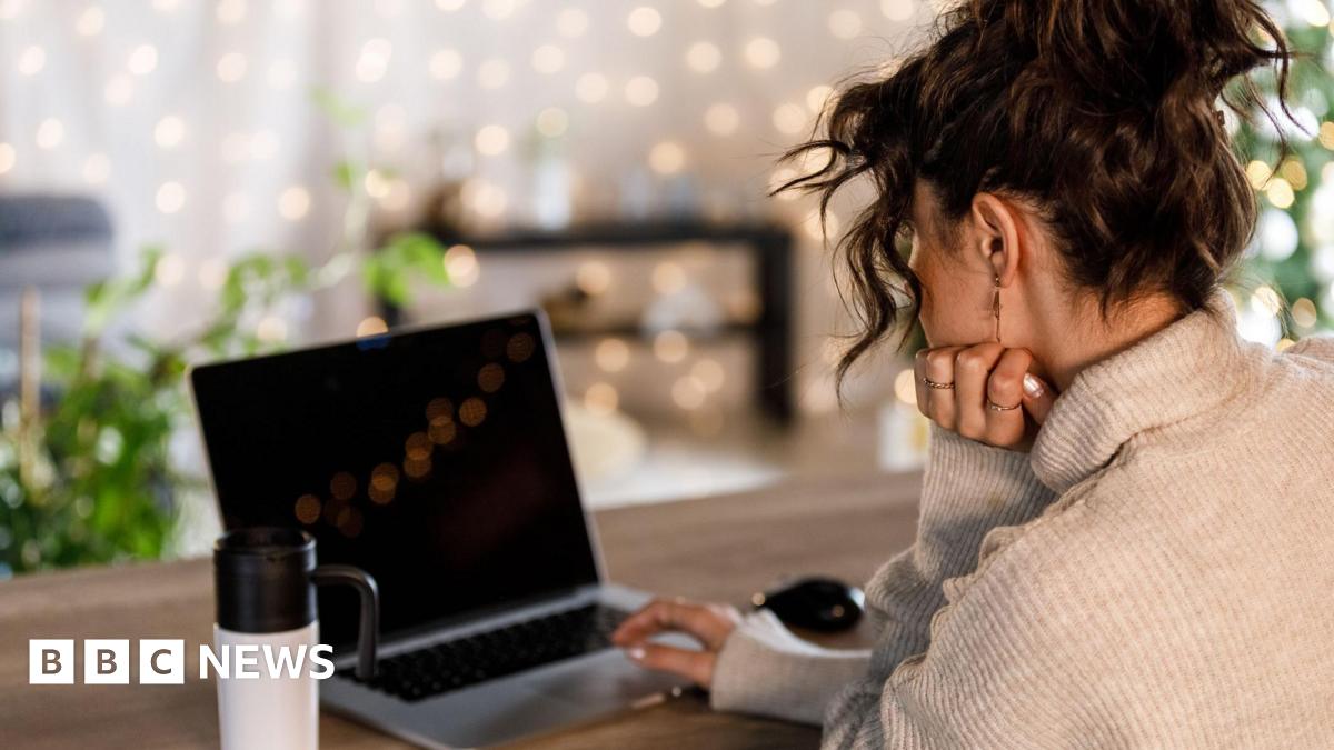 A stock photo shows a young woman sat at a wooden table with an open laptop, resting their chin on one hand. A reusable travel mug sits nearby.