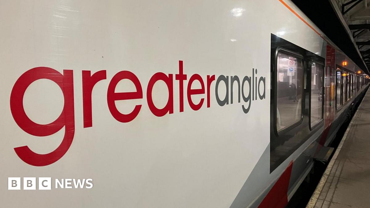 Close up image of a Greater Anglia train - looking along the platform with the company's red and grey logo on the side of the train taking up most of the image.