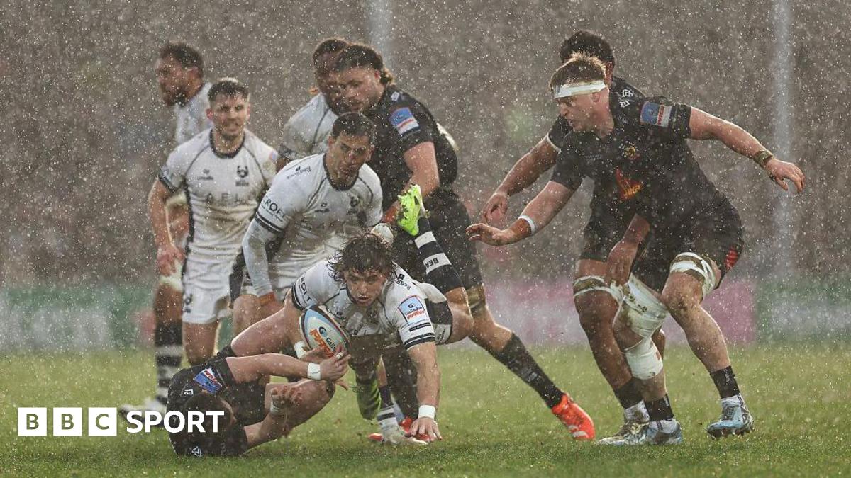 Bernhard Janse van Rensburg powers forward in a rainstorm as various Bristol Bears and Exeter Chiefs players look on.