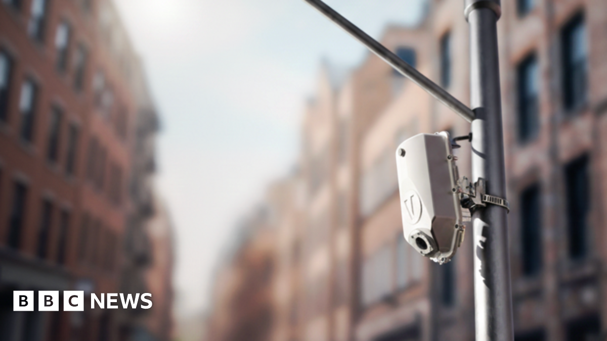 A sensor mounted on a poll with blurred brown buildings seen in the background.