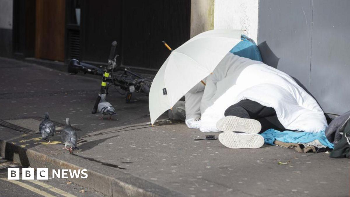 A homeless person covered under a white blanket and white umbrella.