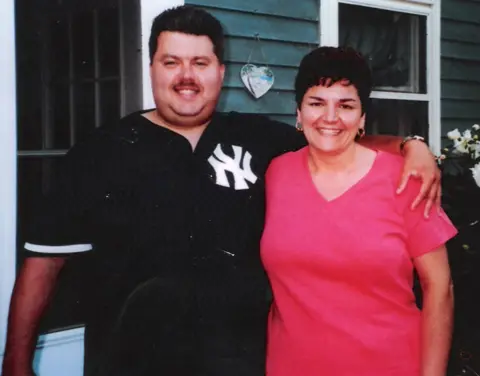 Gina Russo with her then-fiance Fred Crisostomi, pictured in 2002 before the fire. They are smiling with Fred wearing black and Gina pink. Fred has his arm around Gina's shoulders.