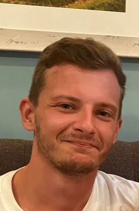 Williams family A young man with short brown hair and a white T-shirt smiles at the camera