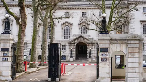 PA Media The grand, cream Inner London Crown Court building with an arched entrance, ornate windows and black iron gates at the front, flanked by trees and a security booth.