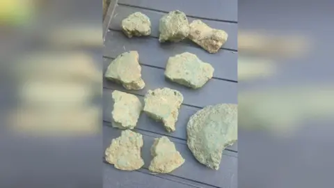 Simon Weller Several lumps of old metal are laid out on a table. 