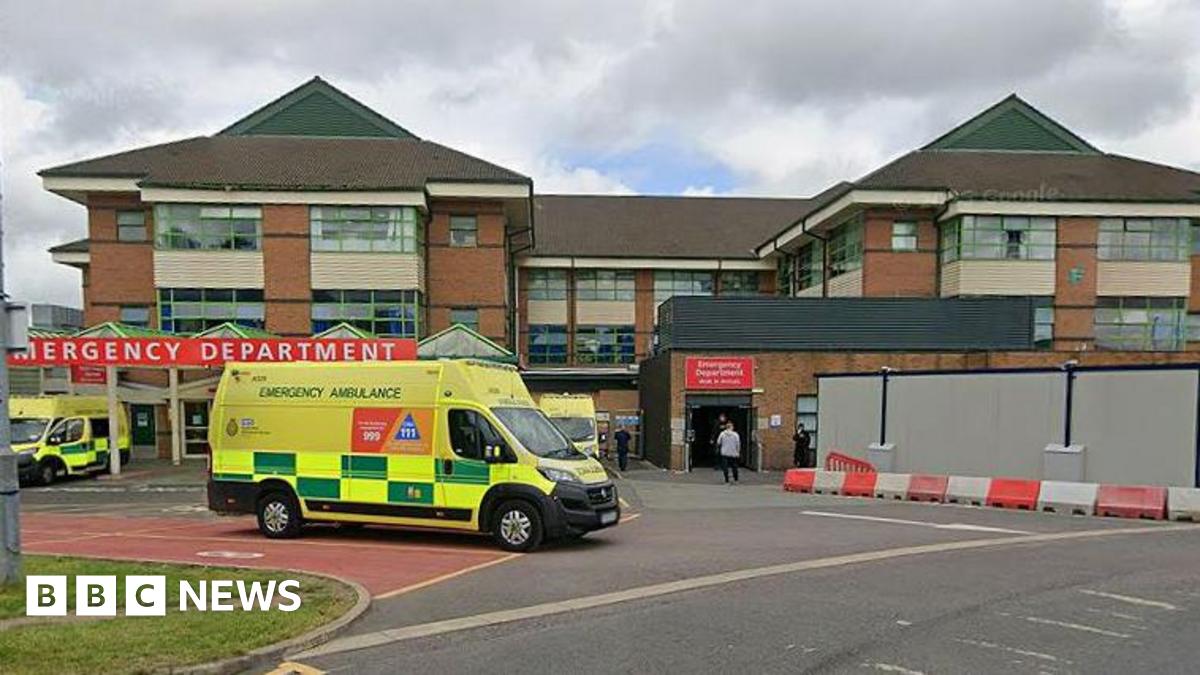 The Accident and Emergency department at the Royal Bolton Hospital. There are ambulances parked outside the building and one appears to be driving away. The ambulances are bright fluorescent yellow with green checks.