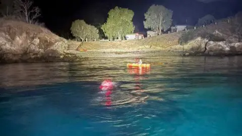 Chris Murray An area of open water pictured in darkness with land and trees in the background. 