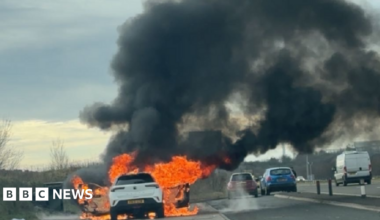 The white car completely damaged by the fire. All the windows have gone and there is debris around the vehicle.