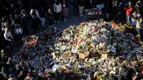 EPA Mourners gather around flowers and candles to commemorate the victims of the fire at the "Le Constellation" bar