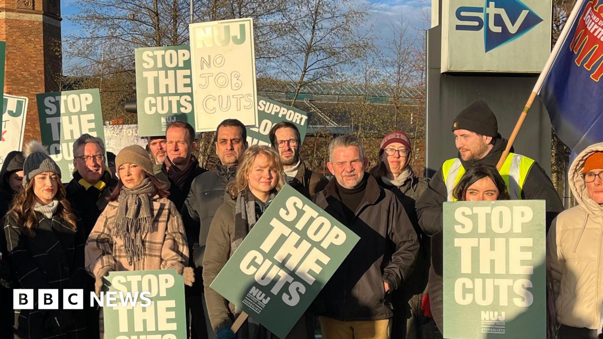 STV staff wearing winter clothing holding placards on a picket line in Glasgow. The signs read "Stop The Cuts" and "No Job Cuts".